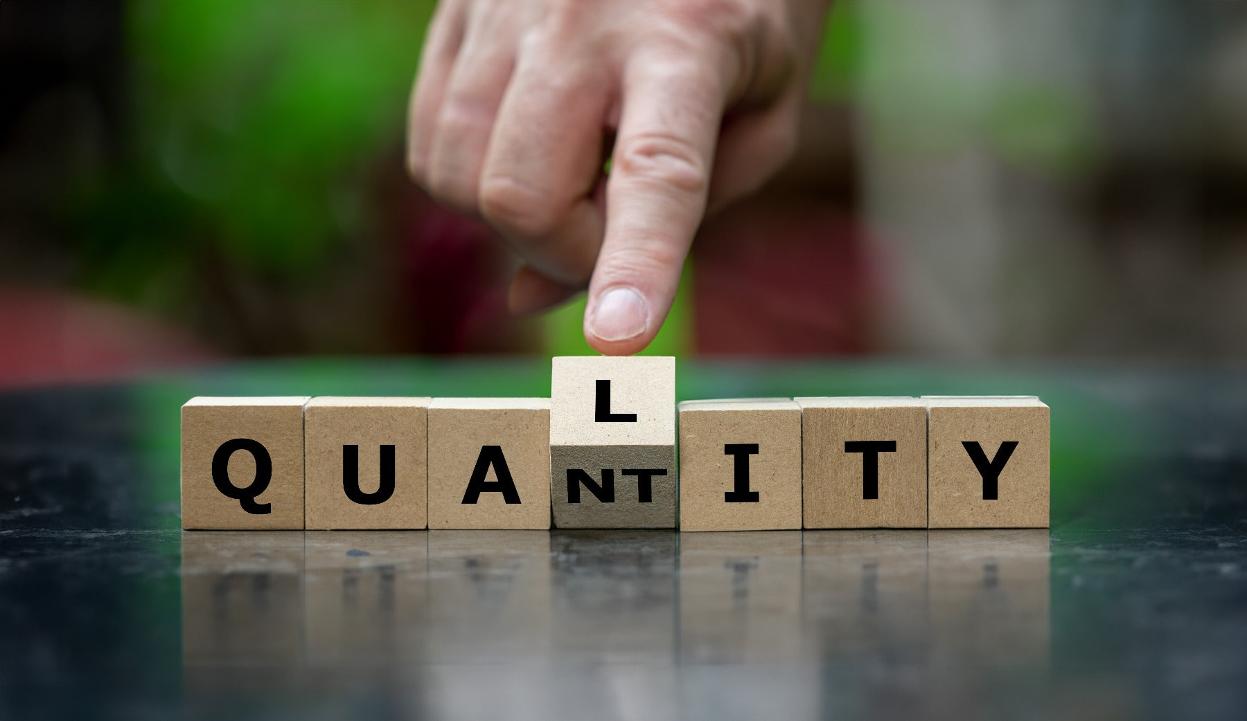 A hand turns wooden cube and changes the word quantity to quality